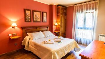 Una cama bien hecha con una colcha color beige, dos almohadas y una mesita con un arreglo floral.