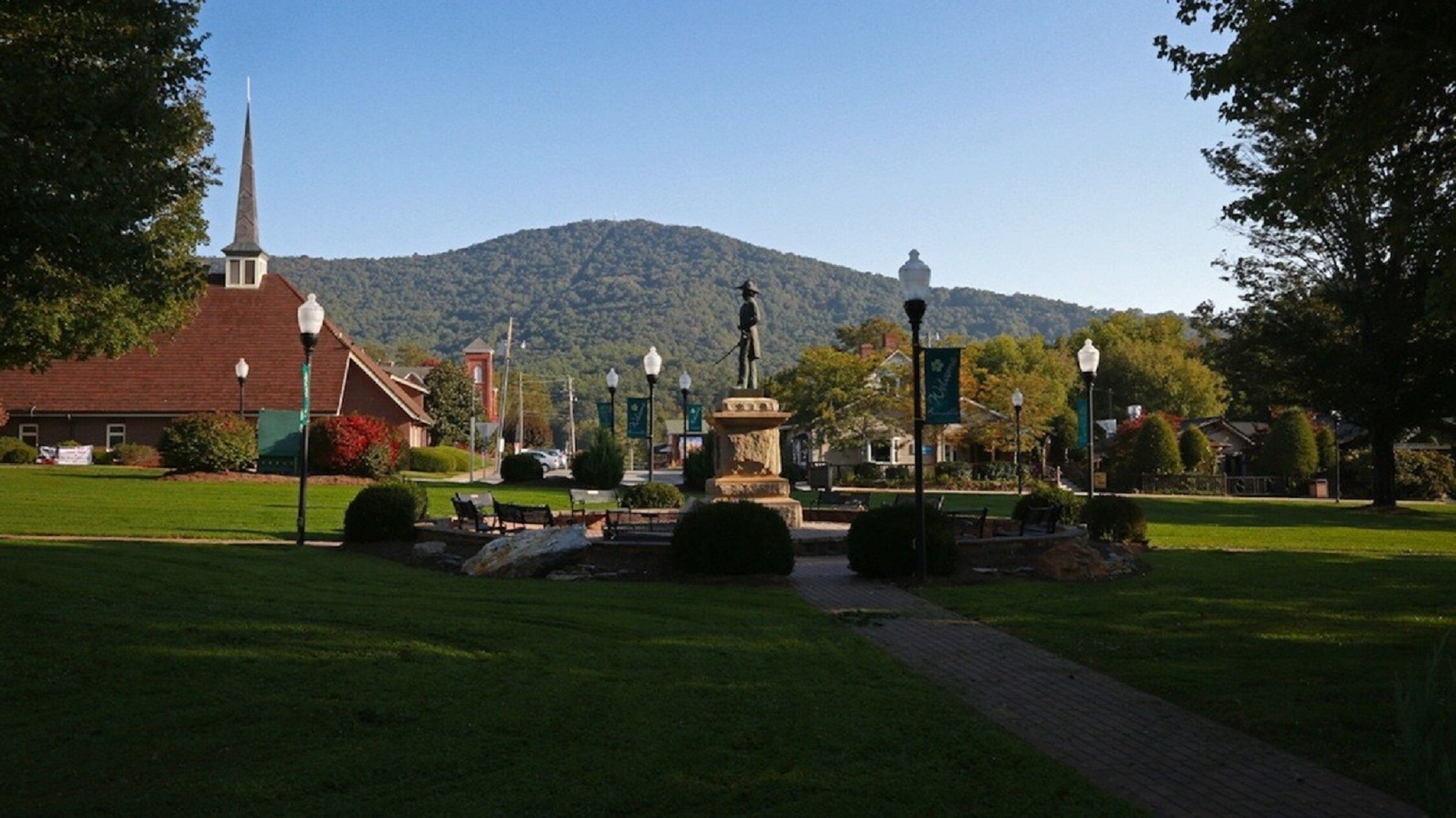 Un parc avec une statue, une église et une montagne en arrière-plan.