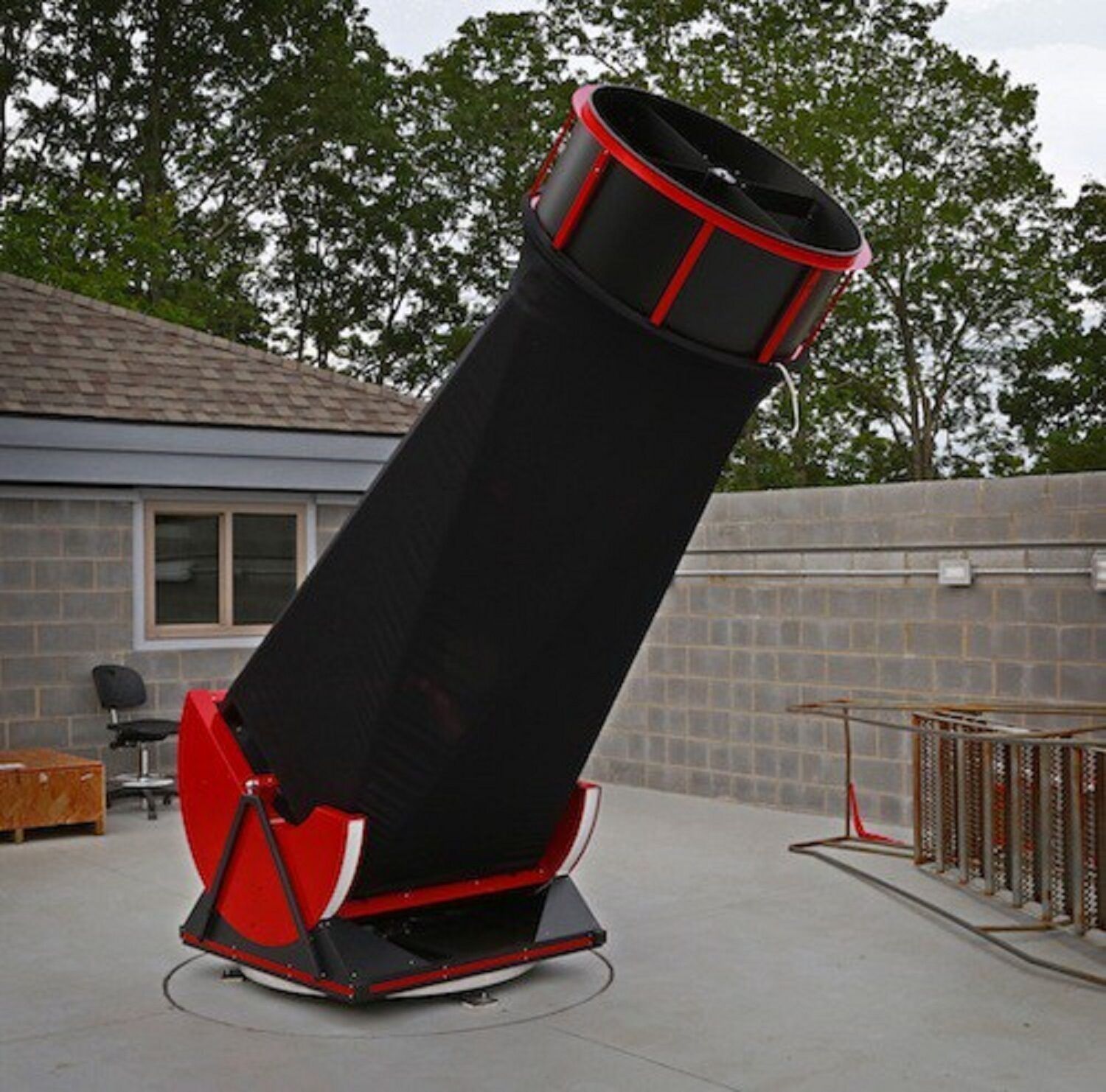 A large, black and red telescope mounted on a stand outdoors.