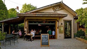 An outdoor seating area with tables and chairs, a chalkboard sign welcoming to SNAP DRAGON, and a building with a sloped roof and wooden siding.