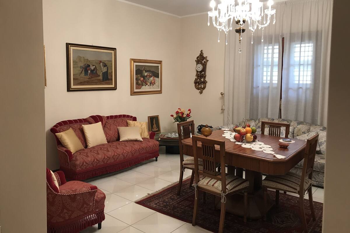 A dining area with a wooden table and chairs, a chandelier, and two framed artworks on the wall.