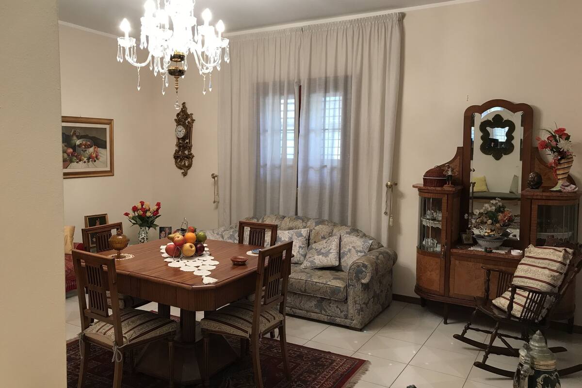 A dining area with a wooden table and chairs, a chandelier, a sofa, and a rocking chair.