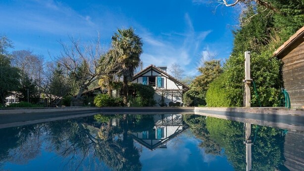 A house with a pool reflecting trees and a clear sky.