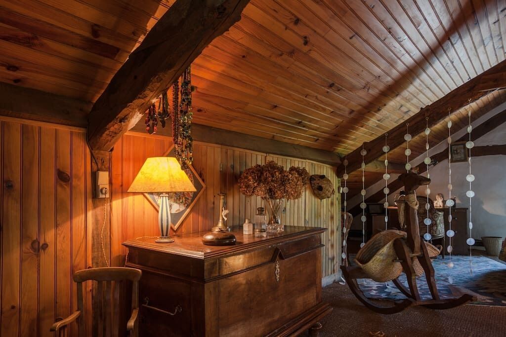 Une pièce mansardée chaleureuse avec des poutres apparentes, une commode en bois, un fauteuil à bascule et des décorations suspendues.