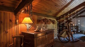 A cozy attic room with wooden beams, a wooden dresser, a rocking chair, and hanging decorations.