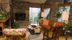 Una sala de estar acogedora con chimenea de piedra, muebles con estampado floral y vistas al exterior.