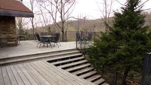 Una terraza de madera con mobiliario exterior, un edificio de piedra y un letrero que indica un sendero de senderismo a 1.6 kilómetros.