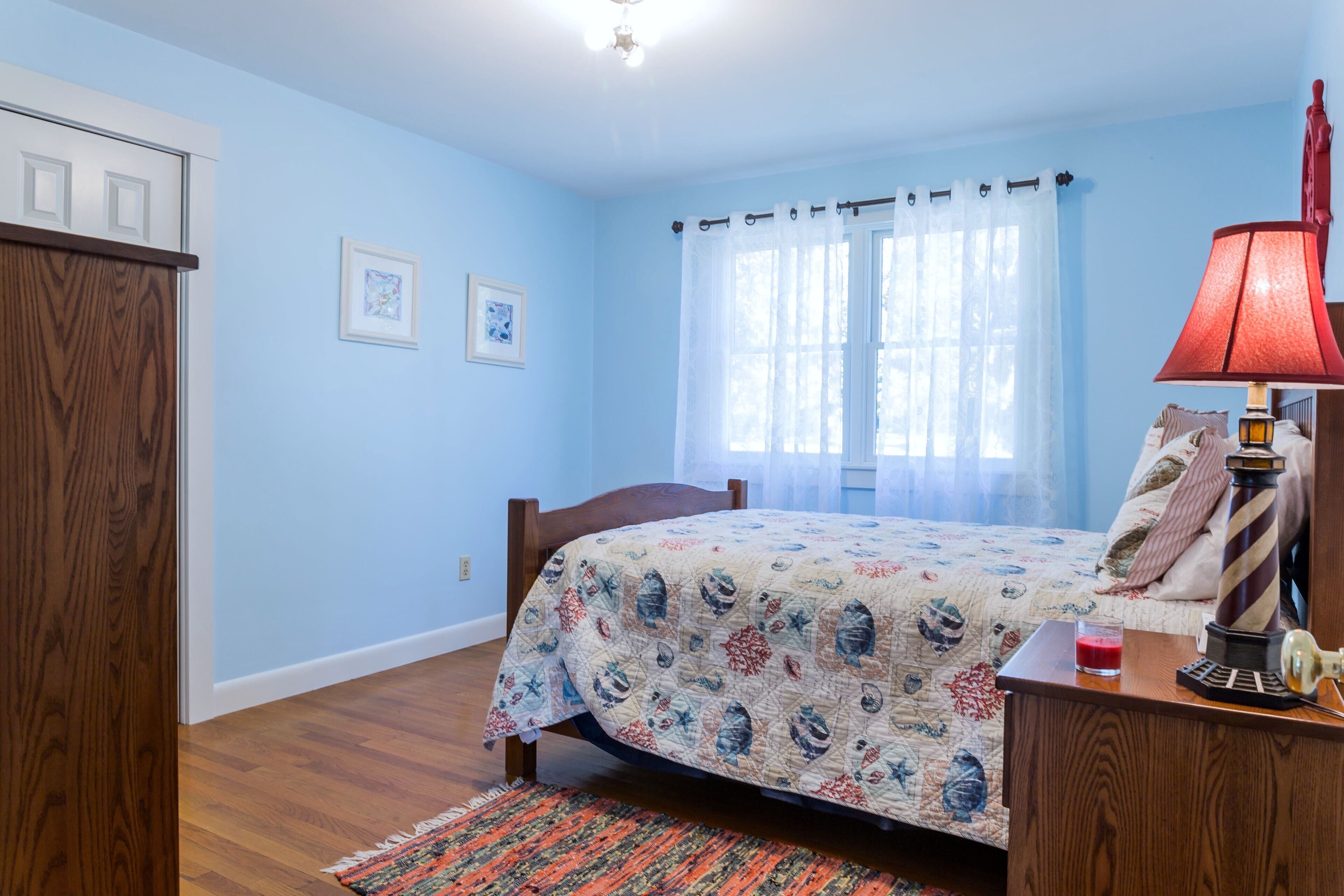 A bedroom with a bed, a wooden wardrobe, a nightstand with a lamp, and a window with curtains.