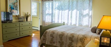 A bedroom with a bed, a dresser, a television, and a window with curtains.