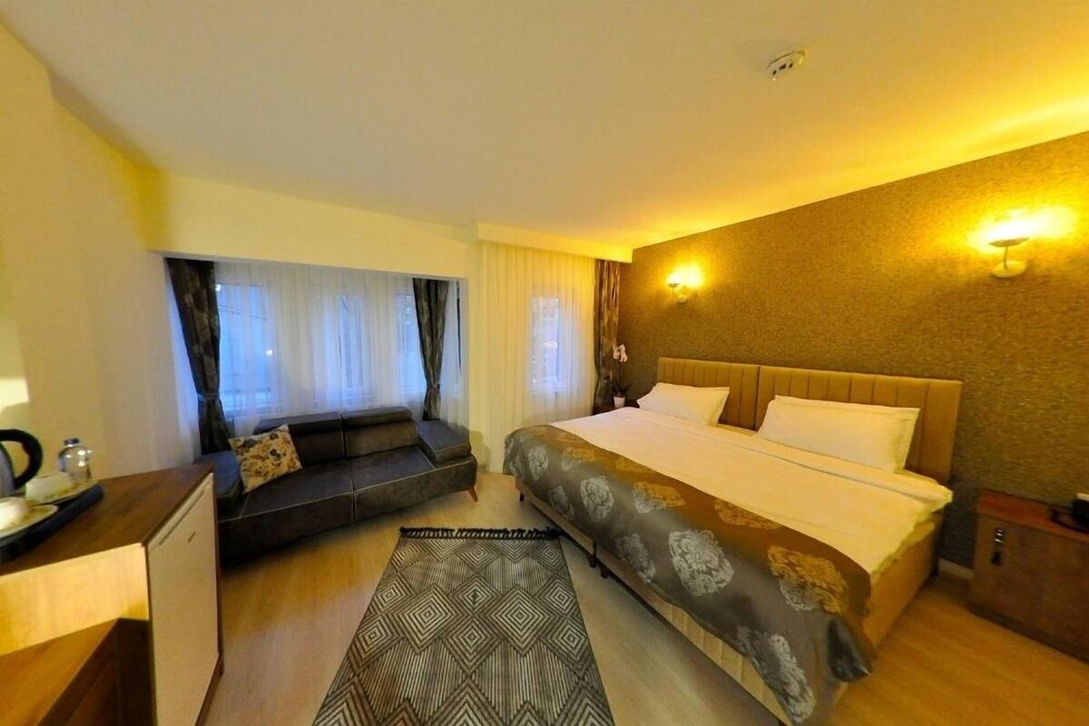 Een hotelkamer met een bed, een bank, een bureau en een raam met gordijnen.
