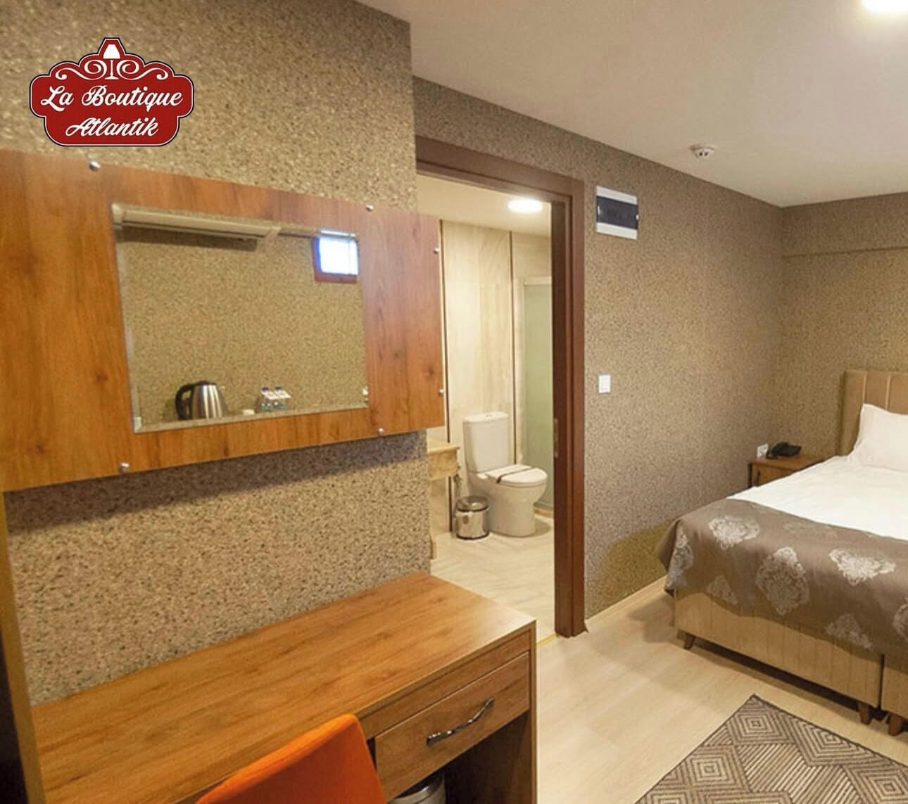 A hotel room with a wooden desk, a bed with a patterned bedspread, a large mirror, and a bathroom visible through an open door.