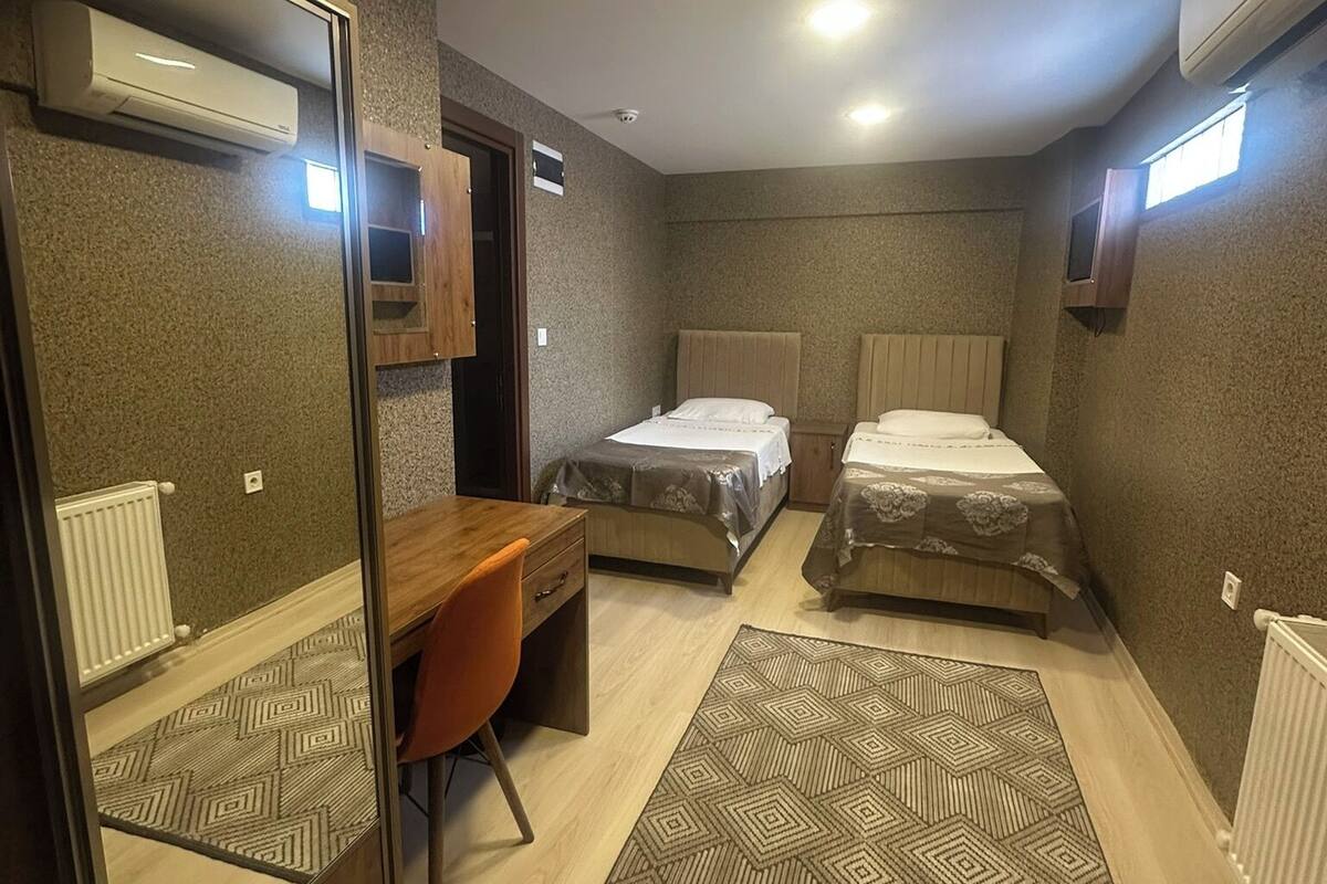 Een compacte hotelkamer met een spiegelkast, een bureau, twee eenpersoonsbedden, een kamerbreed tapijt met dessin en ingebouwde airconditionings.'