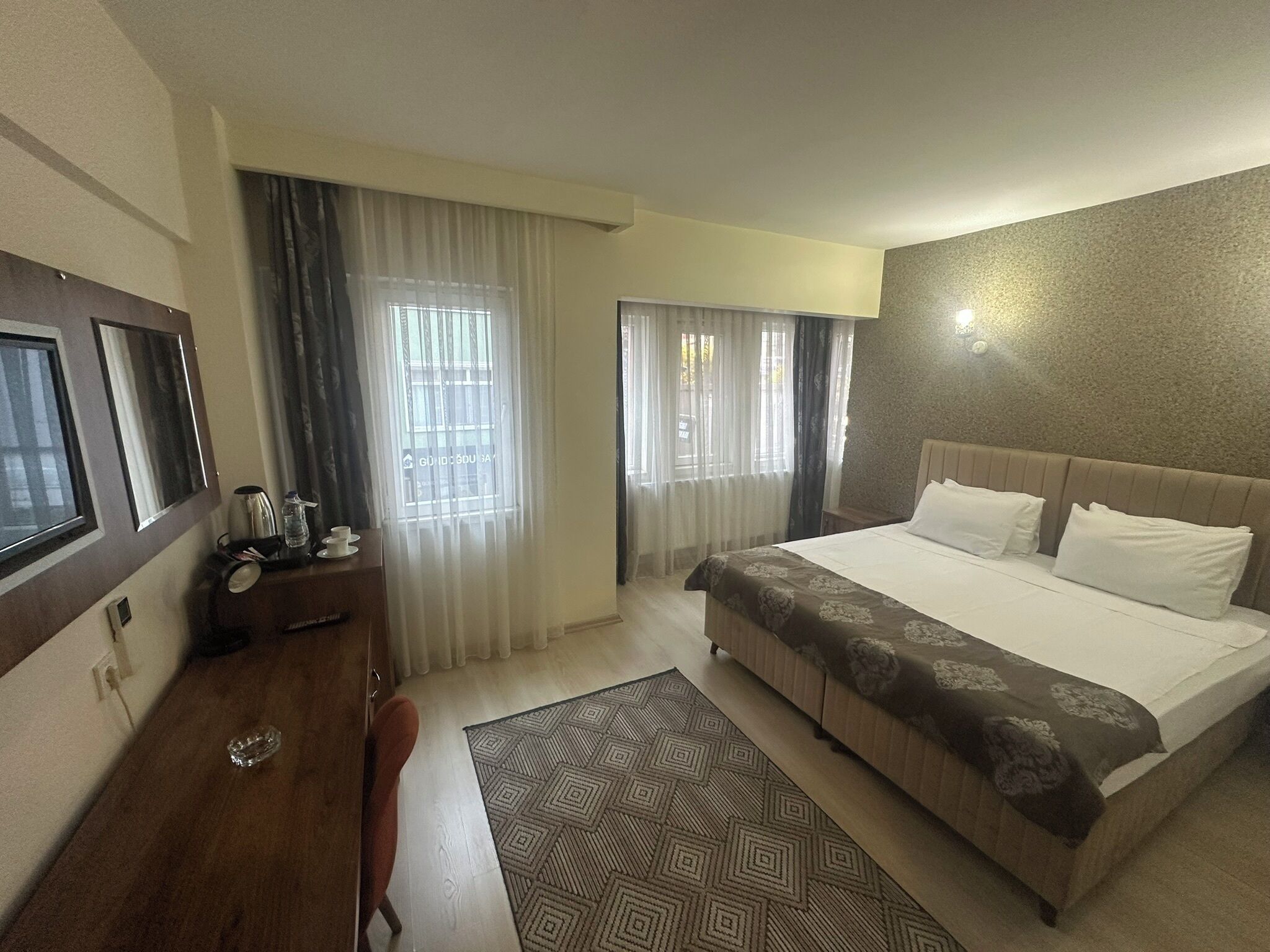 Habitación de hotel con una cama grande, un escritorio con silla, cafetera y ventana con cortinas.