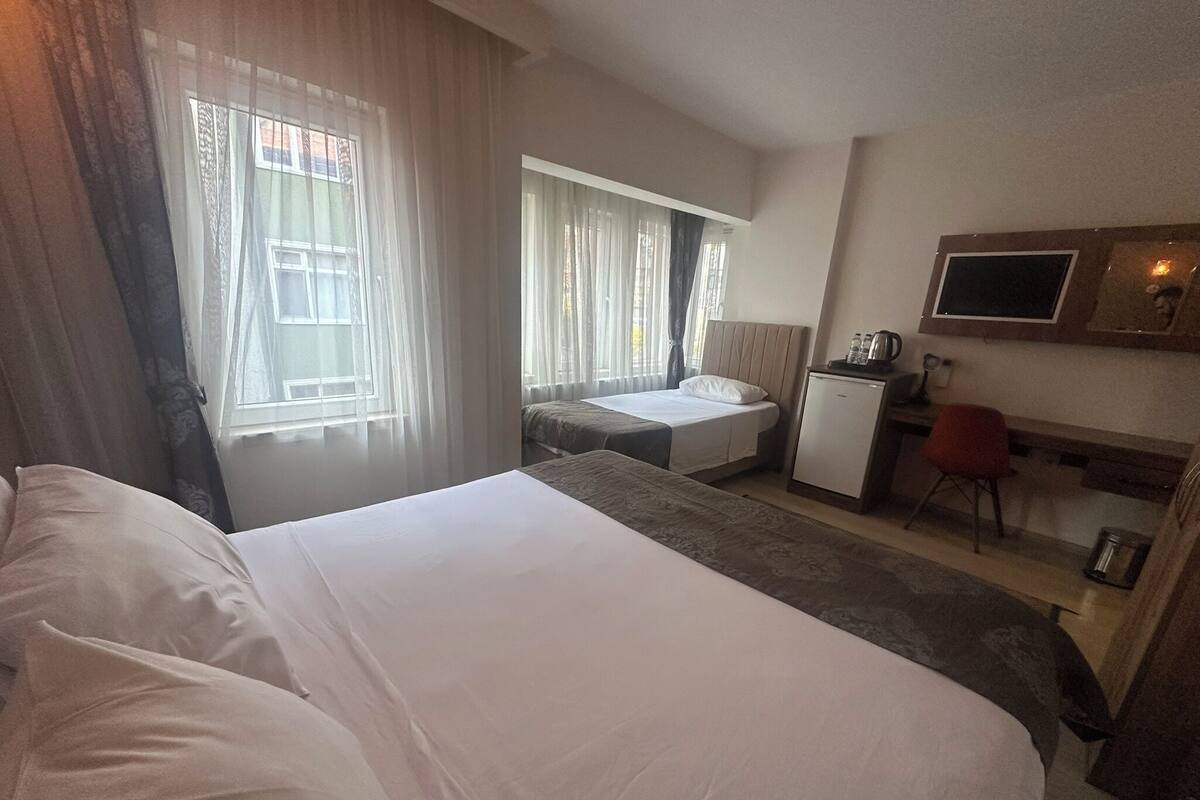 Een hotelkamer met een groot bed, een bureau met stoel, een kleine kitchenette en een aan de muur bevestigde televisie.