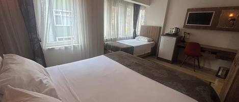 Habitación de hotel con una cama grande, un escritorio con silla, una kitchenette pequeña y un televisor montado en la pared.