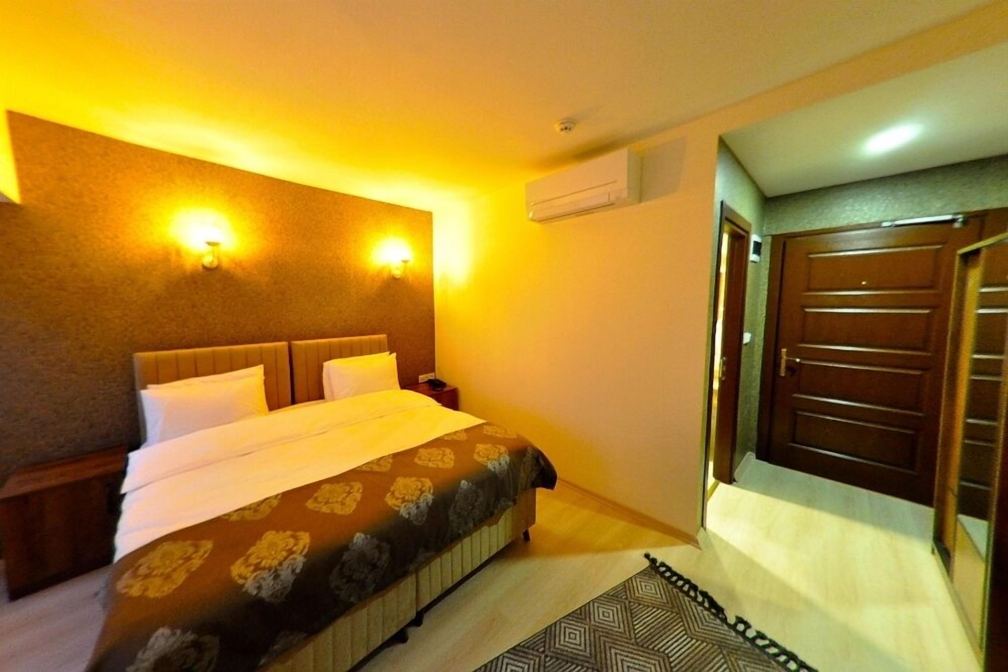 Une chambre d’hôtel avec un grand lit, deux tables de chevet, un climatiseur fixé au mur et une porte avec une poignée.