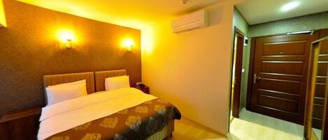 Une chambre d’hôtel avec un grand lit, deux tables de chevet, un climatiseur fixé au mur et une porte avec une poignée.