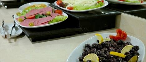 Un bufé con diversos platos, incluyendo ensaladas, carnes y aceitunas negras con rodajas de limón.