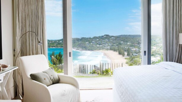 A bedroom with a large window overlooking a beach and a view of a hillside town. - The Elysium by Contemporary Hotels (Palm Beach)