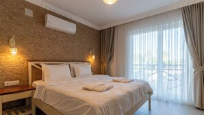 Un lit bien fait, avec du linge de lit et des serviettes blanches, une table de chevet en bois, un mur en briques et une grande fenêtre avec des rideaux.