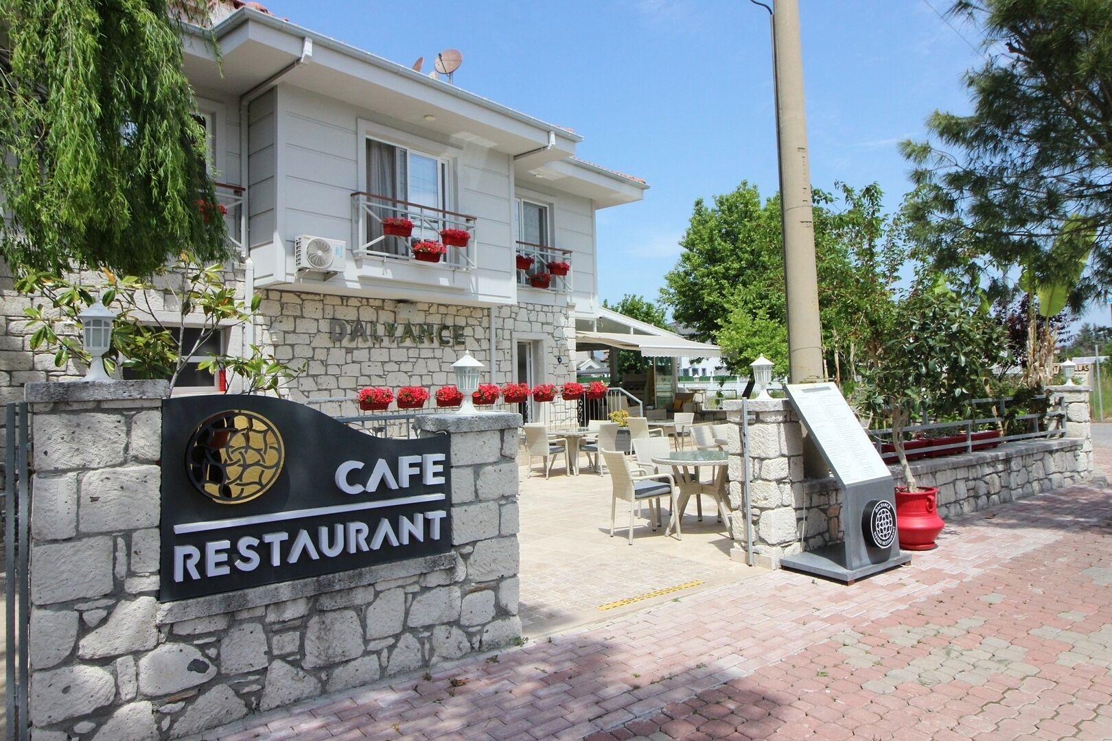 A stone wall with a cafe restaurant sign, outdoor seating, and a stone building with balconies.