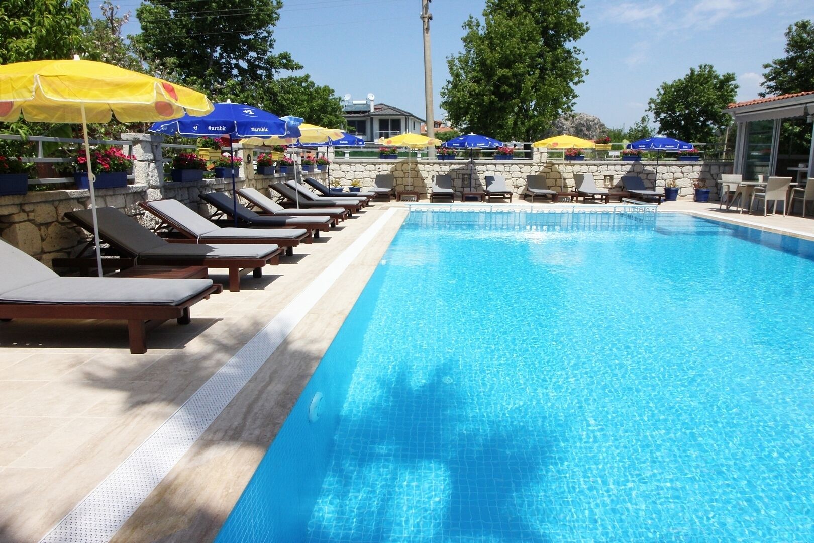 A swimming pool with sun loungers and umbrellas, surrounded by stone walls and potted plants.