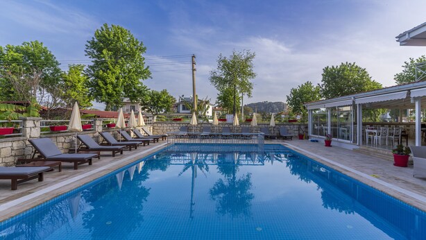 Une piscine rectangulaire, agrémentée de chaises longues et de parasols, entourée de murs en pierre et de plantes en pot.