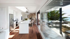 A modern kitchen with a central island, wooden flooring, and a view of a balcony with outdoor seating. - Northview Villa by Contemporary Hotels (PALM BEACH)