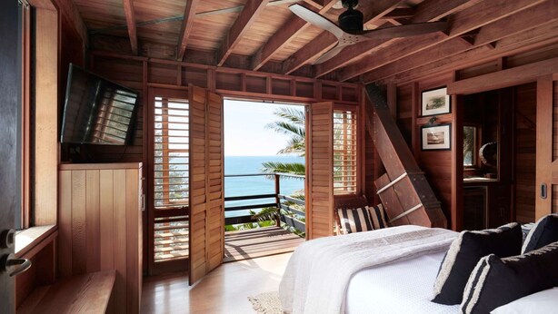 A bedroom with a wooden ceiling, a bed with white bedding, a TV, and a view of the ocean. - Northview Villa by Contemporary Hotels (PALM BEACH)