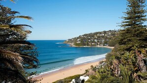 A coastal view with a sandy beach, clear blue sea, and a hillside with houses. - Northview Villa by Contemporary Hotels (PALM BEACH)