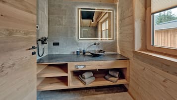 A compact bathroom with a wooden interior, a granite countertop, a large mirror, a sink, and a window.