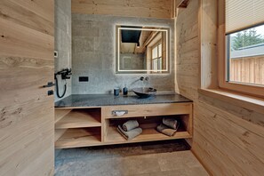 A compact bathroom with a wooden interior, a granite countertop, a large mirror, a sink, and a window.