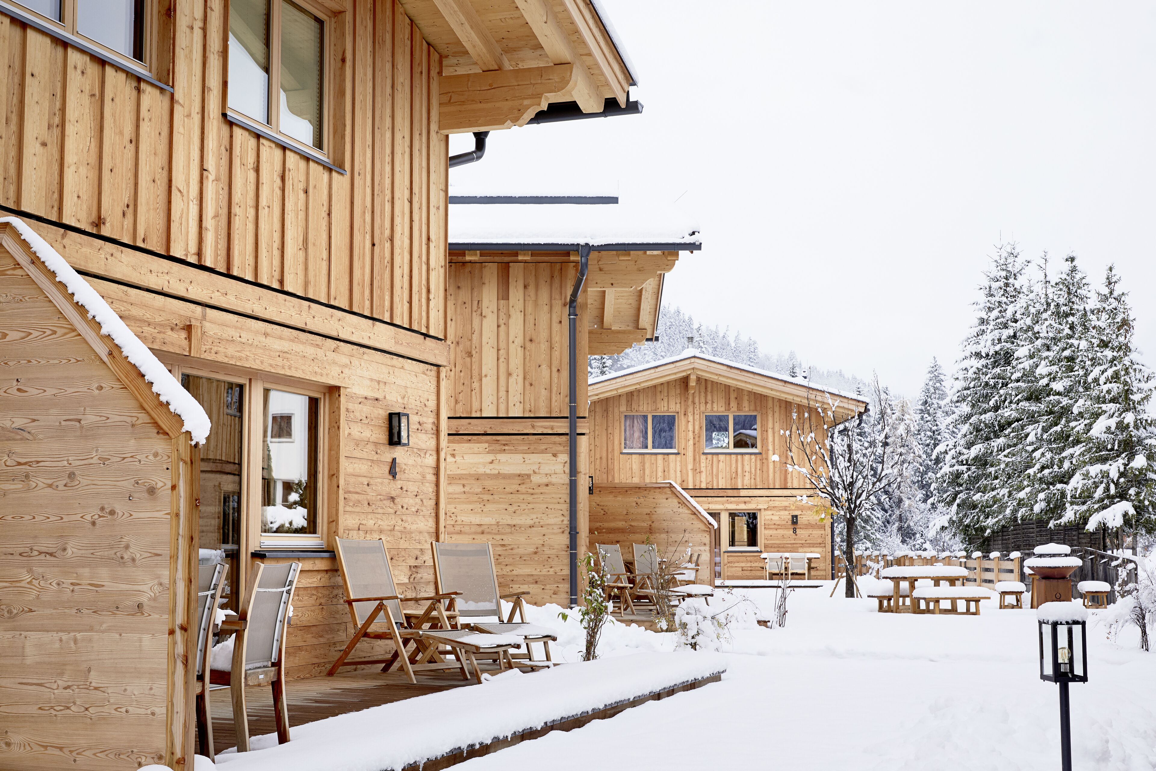 A wooden cabin with a covered outdoor seating area and a snow-covered landscape.