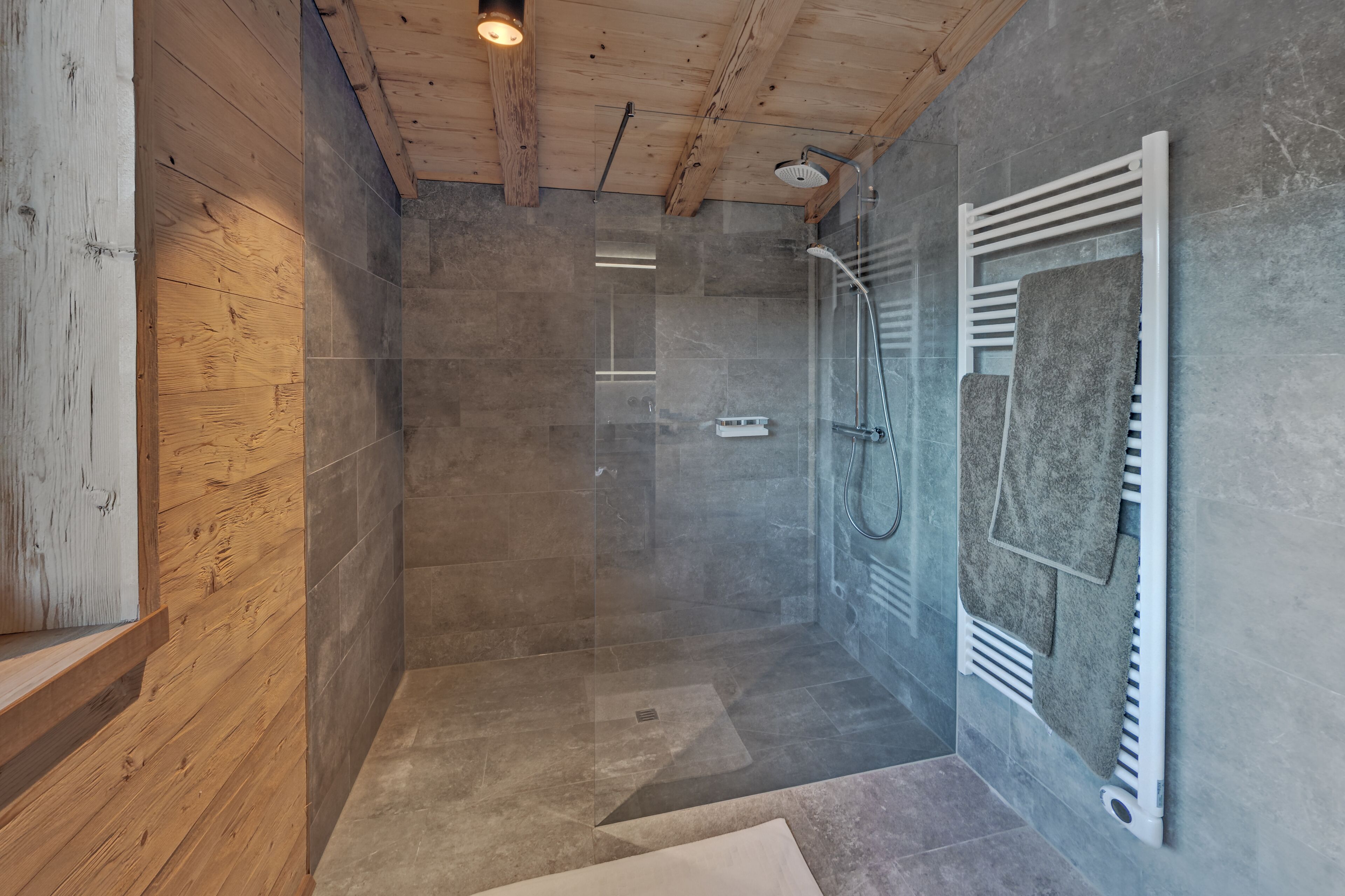 Un espacio de ducha moderno con puerta de vidrio, vigas de techo de madera y un perchero para toallas.