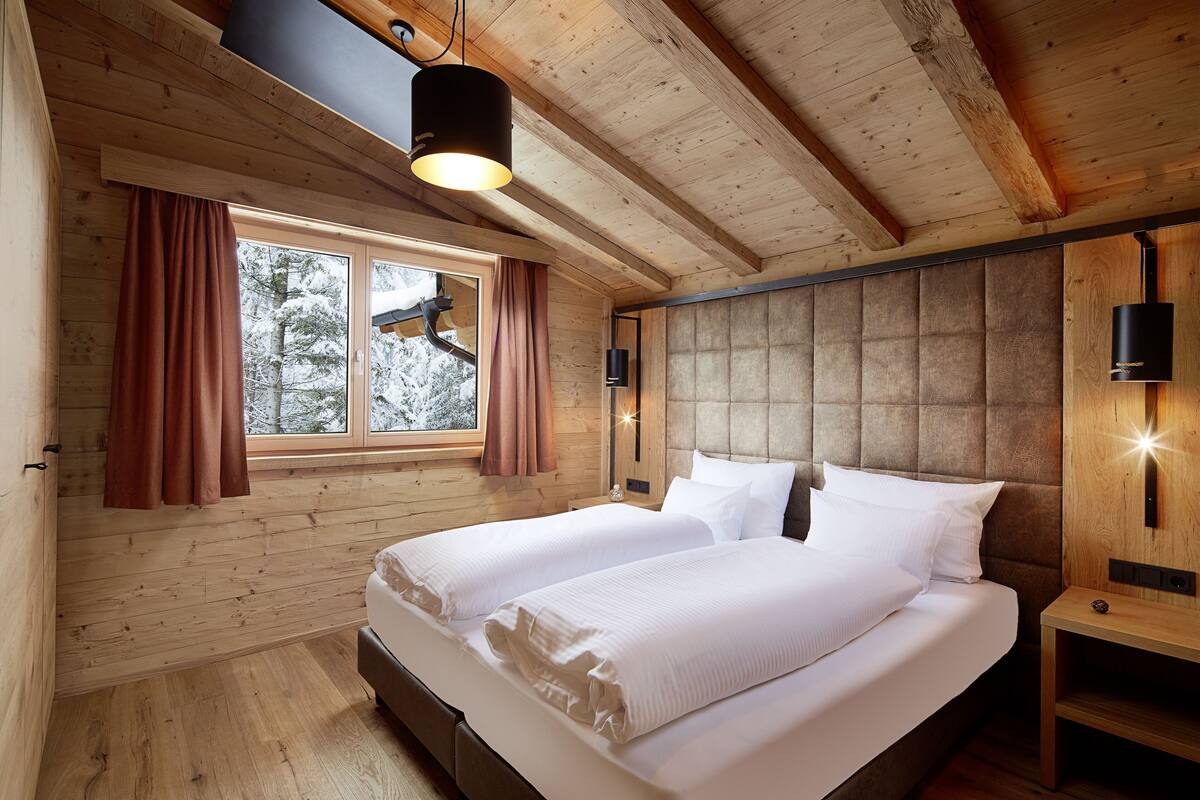 A wooden cabin bedroom with a large bed, two windows, and a ceiling light.