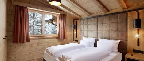 Un dormitorio de cabaña de madera con una cama grande, dos ventanas y una lámpara en el techo.