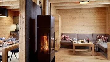 A cozy cabin interior with a wood-burning stove, a dining area, and a seating area with a sofa and table.