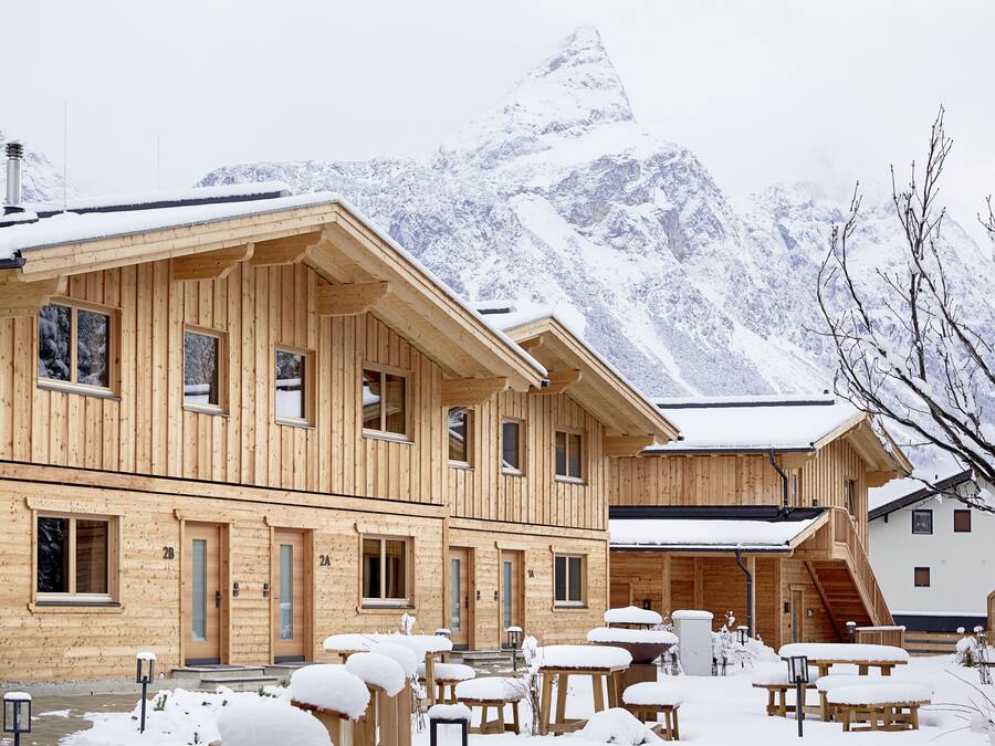Una cabaña de madera con varias habitaciones, un balcón y un paisaje montañoso cubierto de nieve.