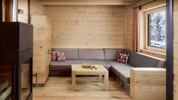 A cozy cabin interior with a wooden floor, a sofa with cushions, a small table, and a window with a view of snow-covered trees.