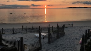 A beach with a fence, a row of beach chairs, and a flag.