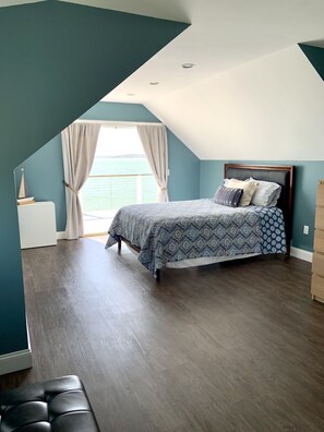 A bedroom with a bed, a nightstand, a window with curtains, and a view of the sea.