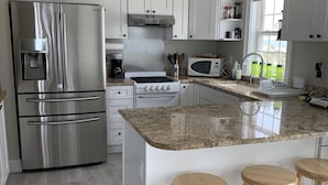 A modern kitchen with stainless steel appliances, white cabinetry, a granite countertop, and wooden stools.