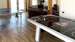 A spacious room with a ping pong table, a leather couch, and a television.