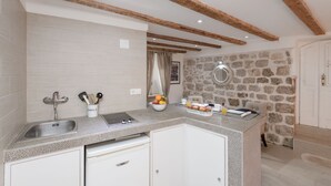 A kitchen with a stone wall, wooden beams, a sink, and a countertop with various items. - Old Town Center Studio Apartments (Dubrovnik)