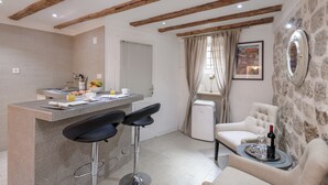 A modern kitchen with a bar area, stone wall, and exposed wooden beams. - Old Town Center Studio Apartments (Dubrovnik)
