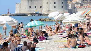 A crowded beach with people sunbathing and swimming, umbrellas, and a historic building in the background. - Old Town Center Studio Apartments (Dubrovnik)