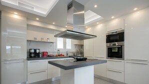 A modern kitchen with a central island, stainless steel appliances, and white cabinetry. - Gem Villa in Viros Corfu  (Corfu)