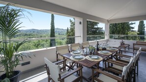 A dining area with a table set for four, surrounded by chairs, on a balcony with a view of a forested landscape. - Gem Villa in Viros Corfu  (Corfu)