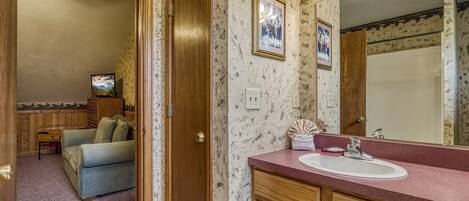 A bathroom with a vanity, mirror, and a television in the adjacent room.