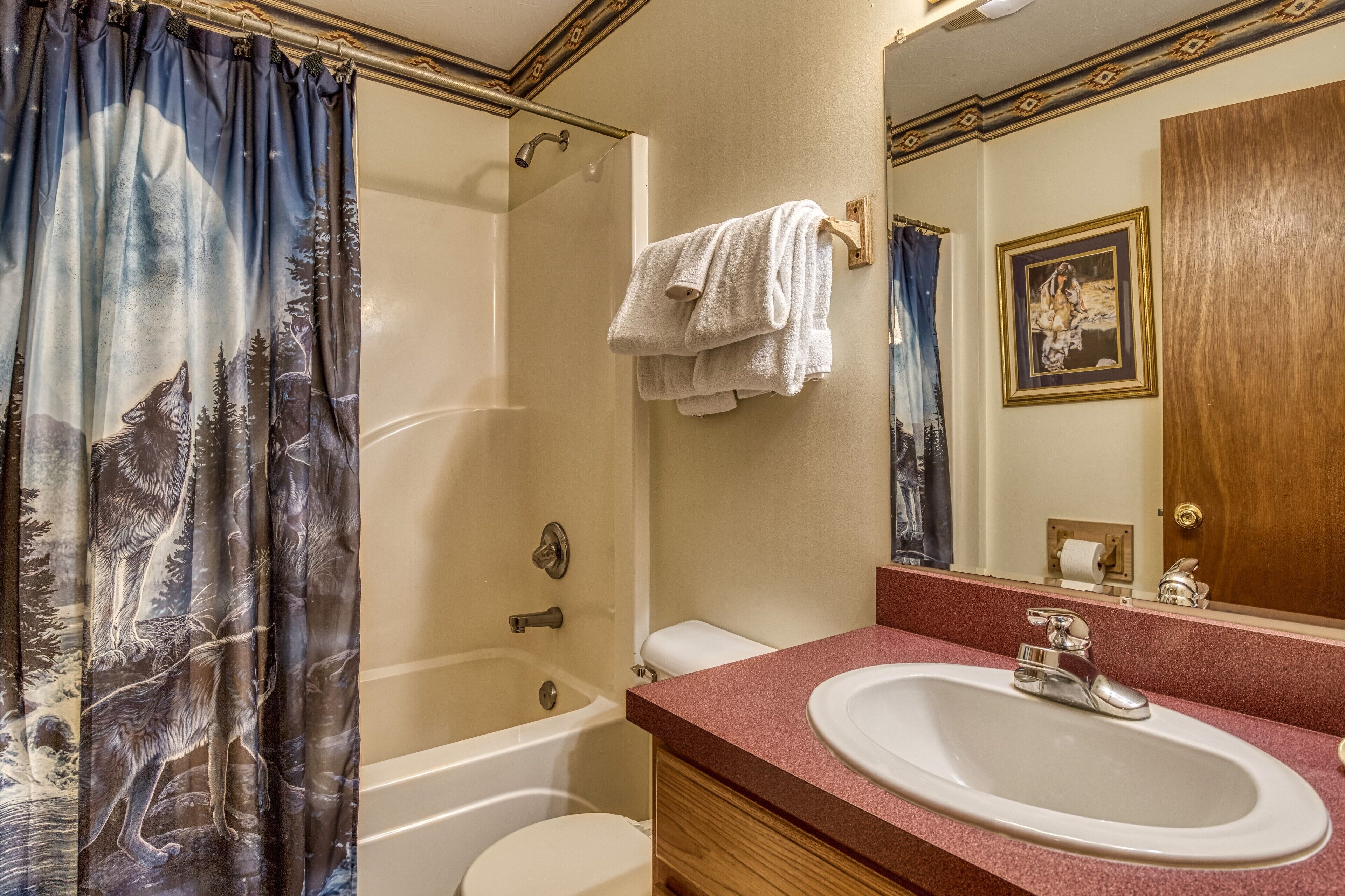 A bathroom with a bathtub, toilet, sink, and a shower curtain with a wolf and forest design.
